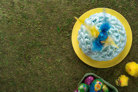 Funny Easter cake decorated with feathers of different colors and colorful eggs Easter food on green...