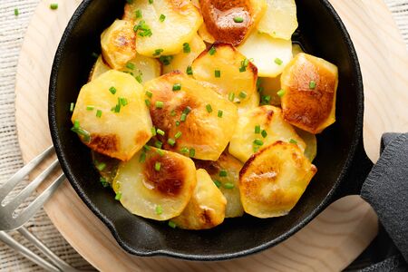 Close up Roasted potatoes slices in iron skillet with herbs. Rustic background, top view. Selective focus. Homemade food. Nutrition concept.の写真素材