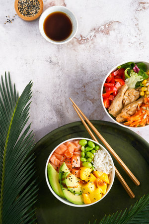 Hawaiian trendy poke bowls with salmon, heura soy protein or vegan chicken, variety vegetables, mango served in bowl on tropical leaves. Marble table, Top view. Healthy Nutrition concept. Copy space.の写真素材