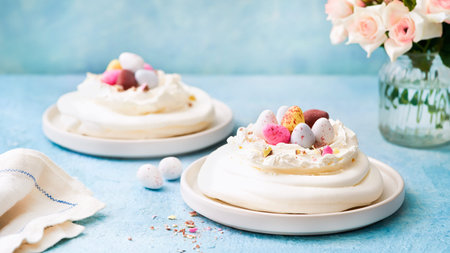 Meringue nest cake with colorful chocolate eggs, buttercream frosting on light blue background with...