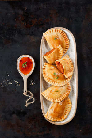 Closeup of typical spanish empanadas, small tuna or meat fried pies, tomato sauce, bell pepper. Dark...