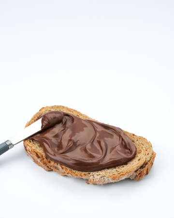 Slice of whole wheat toast with healthy chocolate hazelnut spread, knife on white background with space for text.の写真素材