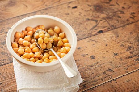 Cooked chickpeas in white bowl on wooden background. Spilled chickpeas. Vegetarian food concept. Macrobiotic diet.の写真素材