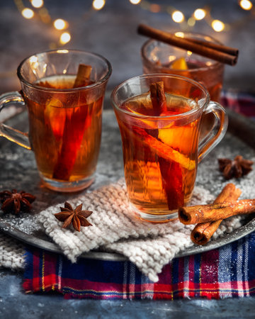 Hot drink for New Year, Christmas or autumn holidays. Mulled cider or spiced punch, tea or mulled white wine with lemon, apples, cinnamon, anise, cloves on a dark backround.の写真素材
