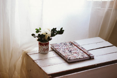 Vase with flowers on a wooden table and a book in the backgroundの写真素材