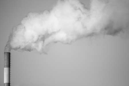 Black and white image. Place for the inscription. Air pollution from the boiler pipe. The chimney smokes against the sky. Ecology concept and bad environment.の写真素材