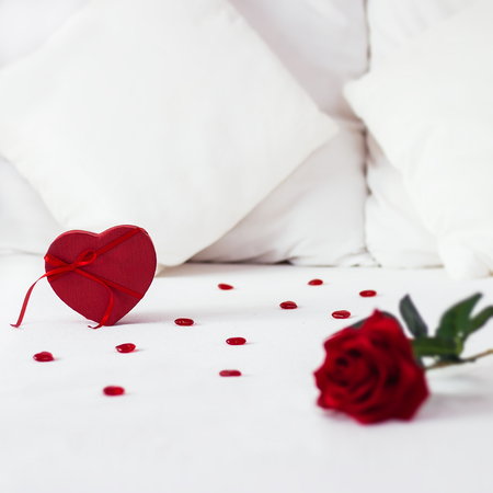 Valentines day surprise at morning on the white bed for her. Red heart gift box background with rose on the front . copy space squareの写真素材