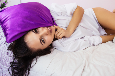 Womans day, morning breakfast white bed, portrait of young brunette girl in pink room Provence style, with purple pillow, book, food, flowersの写真素材