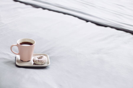 Pink cup coffee, grey plate with donut, on bed. good morning