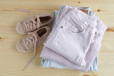 Children s snickers and stack of clothes. Jeans, shirt, kid snickers on wooden table and white background isolation.の写真素材