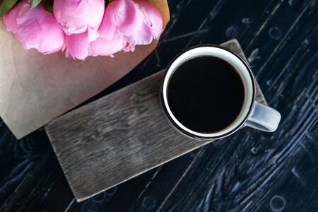 Cup of americano coffee and pink flowers wrapped in kraft paperの写真素材