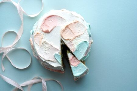 Birthday cake with a slice cut off and pink ribbon on blue background Photoの写真素材
