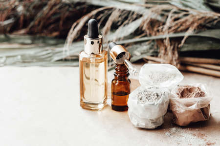 Glass bottles oil and bags of different colors cosmetic clay for face and body care. Palm leaves on background. Natural cosmetics. Photoの写真素材