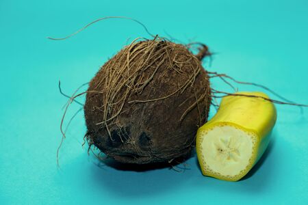 Whole coconut with facial expression lying on turquoise background and cut bananaの写真素材