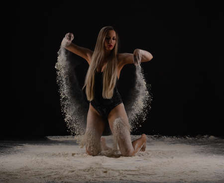 Beautiful sensual fit slim dancer in black body with long blond hair throwing dust, flour, powder on black background.の写真素材