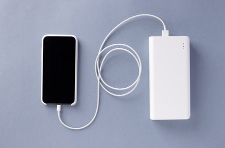 smartphone in a white case is charged from a white Power bank charger. Modern technology. blue...