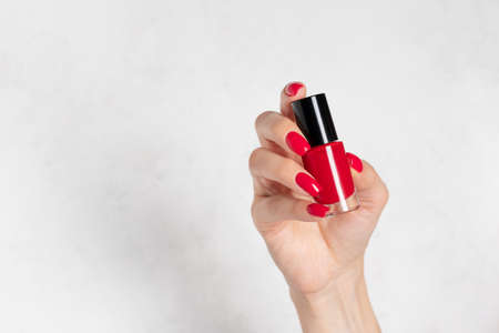 female hand with red nail design holding nail polish bottle. Perfect nailsの写真素材