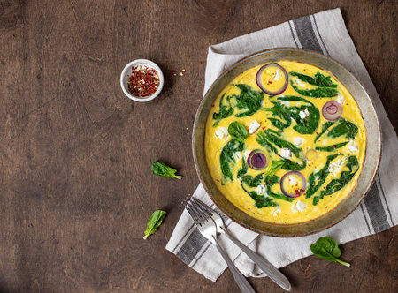 omelet with spinach and feta cheese in an iron pan on a wooden, rustic background. Top view. copy...