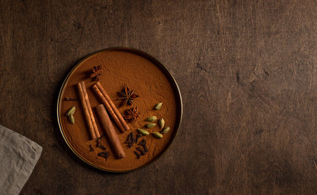 different aromatic spices in a plate. cardamom, cinnamon, cloves, star anise. wooden background, top...