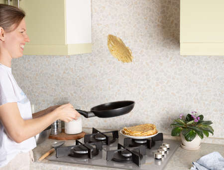smiling woman flipping hot pancakeの写真素材