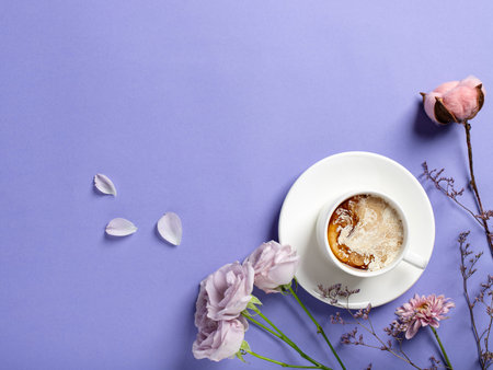 White porcelain cup of coffee and beautiful flowers on a lilac background. morning coffee cup...