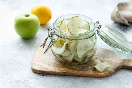 open glass jar with apple chips on wooden board
