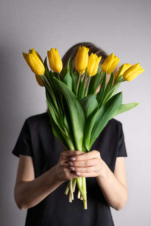 Woman with bouquet of yellow tulips hiding her faceの写真素材