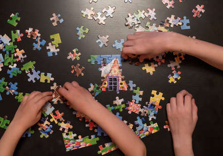 childrens hands collect puzzle on dark table. educational game puzzle. top view. selective focus.の写真素材