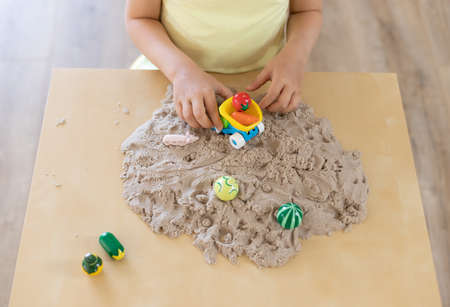 little child playing with kinetic sand and toys at tableの写真素材