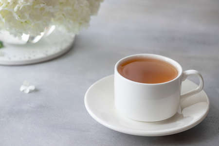 Close-up of a porcelain cup with herbal tea on a blurry background of white flowers. minimalism. horizontal image. gray concrete background.の写真素材