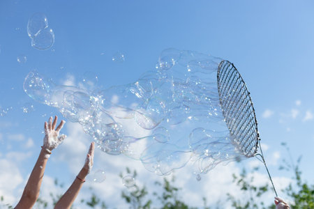 childrens hands catching large soap bubbles against blue skyの写真素材