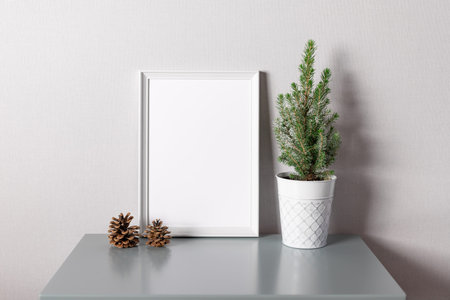 White blank frame and potted christmas tree on table