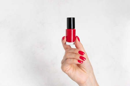 red nail polish bottle in a female hand with red manicure. hand skin care conceptの写真素材