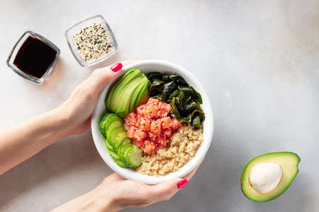 female hand holding bowl with quinoa, salmon, avocado, wakame seaweedの写真素材