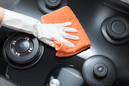 Person hand holding rag and wiping gas stove top