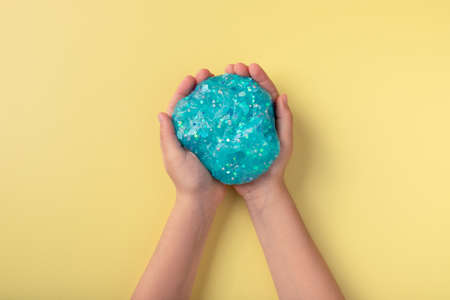 childs hands holding blue glitter slime over yellow backgroundの写真素材