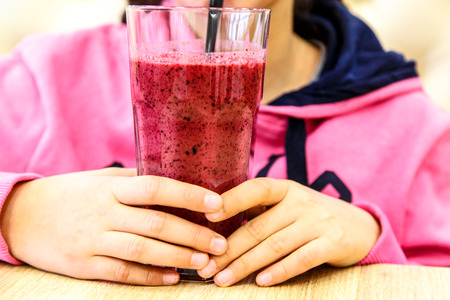 The glass with smoothie in hand, the little girl is drinking through a straw.の写真素材