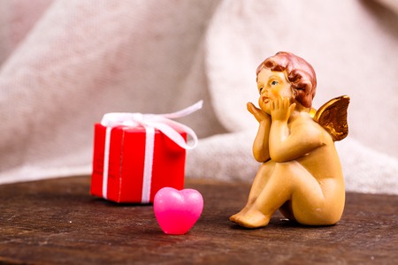 Valentine's day. Little angel is sitting near a red box and a lonely heart.の写真素材