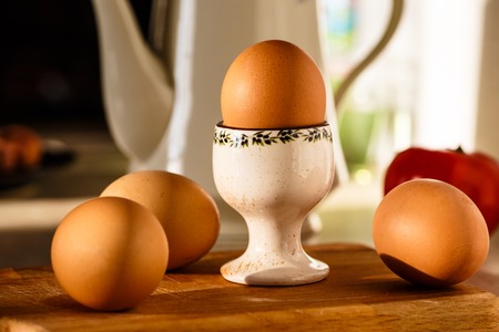 Boiled eggs lit by sunlight and lie on the table. One egg lies on the stand.の写真素材