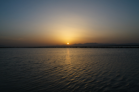 The sun sets behind the mountains behind the lake.の写真素材
