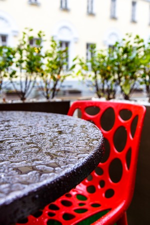 Street cafe in the rain, raindrops on black table and red chair.の写真素材