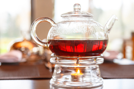 Black tea in glass Cup and glass teapot with a candle stands on the table. A cozy evening at home in the cold season.の写真素材