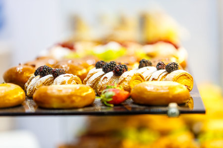 The blackberries are on the roll cake among other sweets on the counter of the pastry shop.
