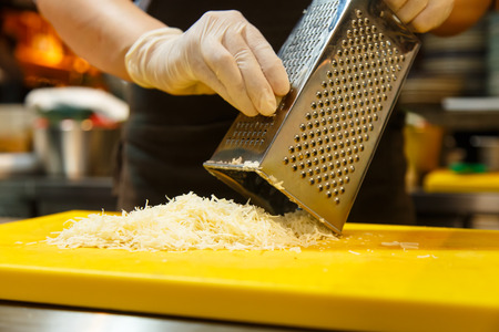 Cook rubs cheese on the grater for pasta or risotto.の写真素材