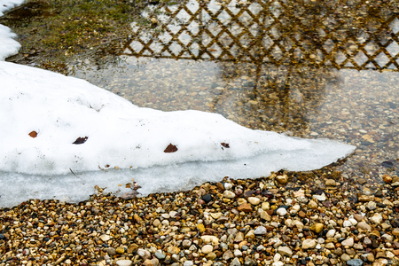 The snow is melting on the banks of puddles. The bottom of colored pebbles in a shallow puddle.の写真素材