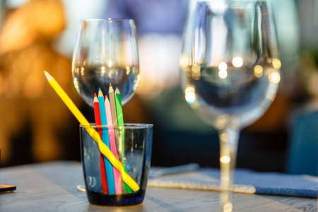 A glass of wine and some pencils is on the table in the restaurant. Illustration for the theme "children in the restaurant."の写真素材