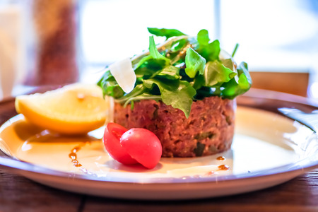 Tartare of beef lying on the plate with arugula, tomatoes and lemonの写真素材