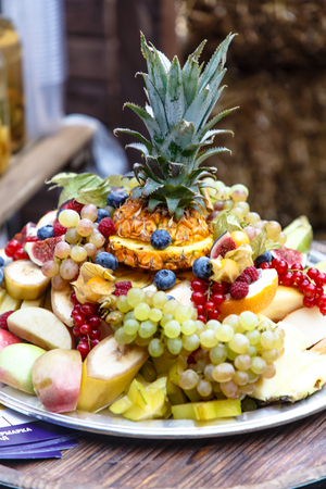 Sliced fruits and berries (pineapple, grapes,apples, bananas, raspberries, blueberries, and others) lie on a plate slide.の写真素材