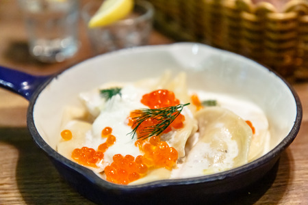 Dumplings  (pelmeni or vareniki) with sour cream and red salmon caviar lie on a frying pan.の写真素材