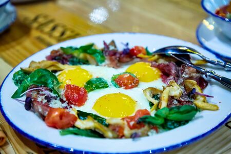 Fried eggs from three eggs with tomatoes, bacon and greensの写真素材